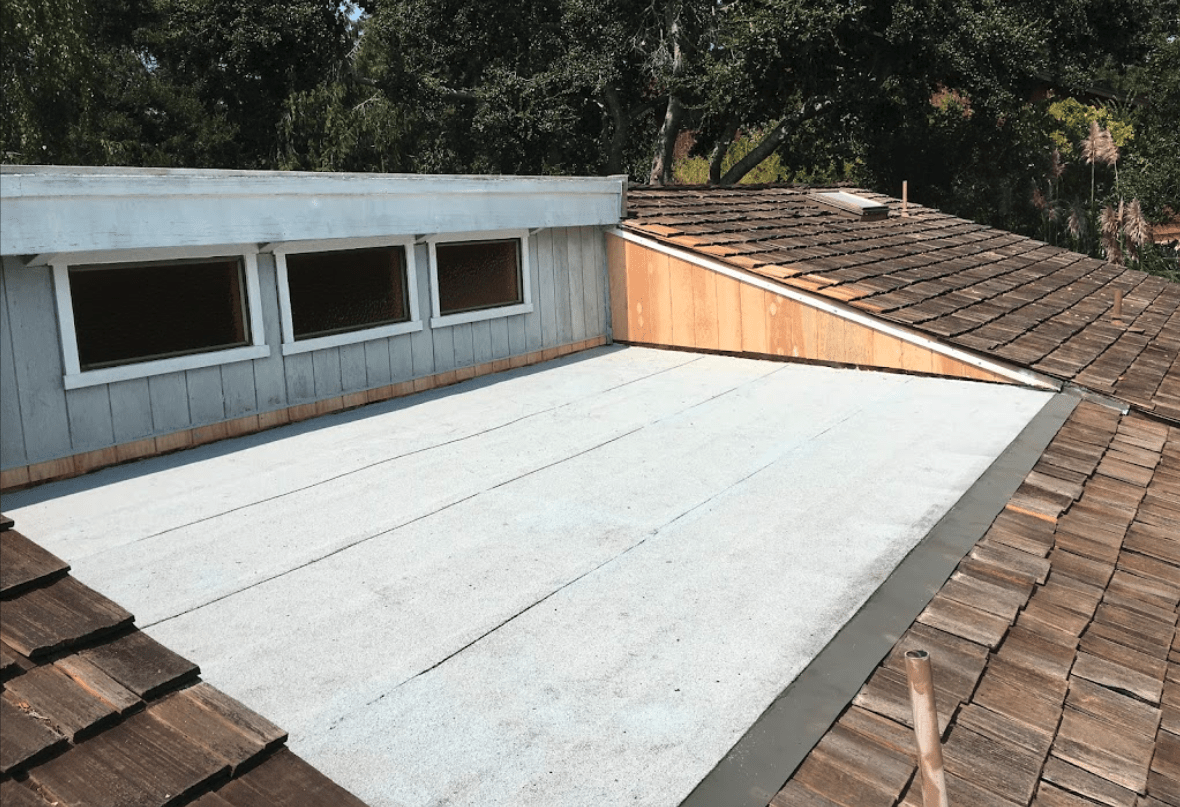 Flat roof replacement in progress beside a wood shake roof