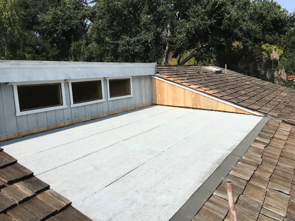 Flat membrane roof beside weathered wood shake roofing during a roof inspection in Capitola, CA